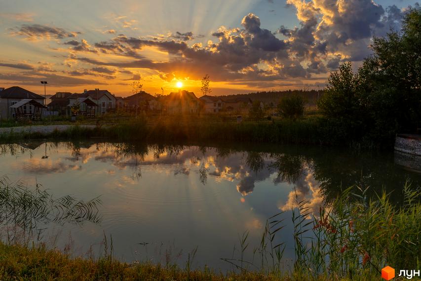 Котеджне містечко КМ Home Resort на фоні заходу сонця з відображенням у воді. Затишні будинки та зелена територія біля озера.