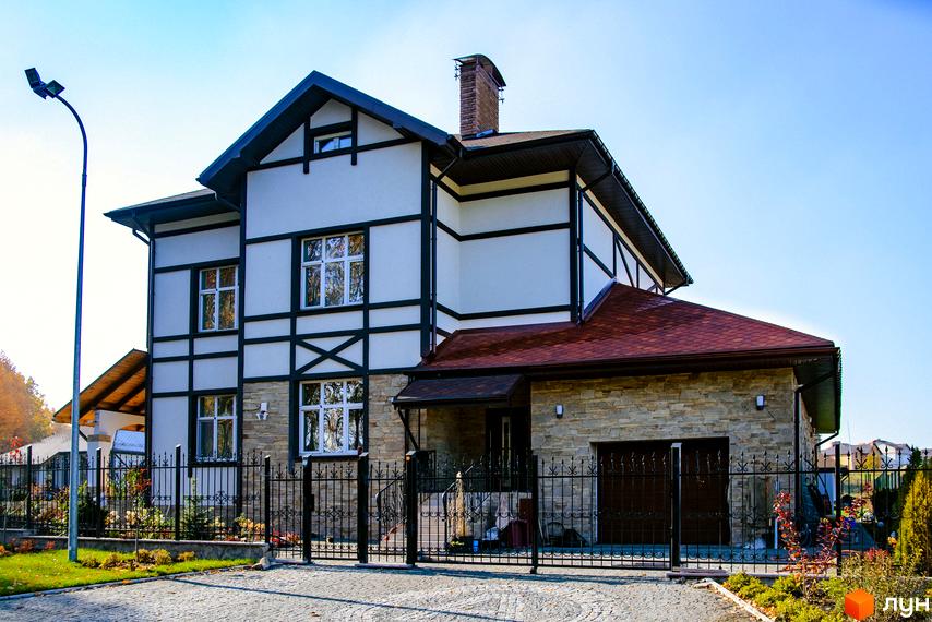 Котеджне містечко КМ Home Resort: двоповерховий будинок з кам'яним цоколем, червоним дахом та оздобленням фасаду під дерево. Огороджена територія з кованою огорожею та ландшафтним дизайном.