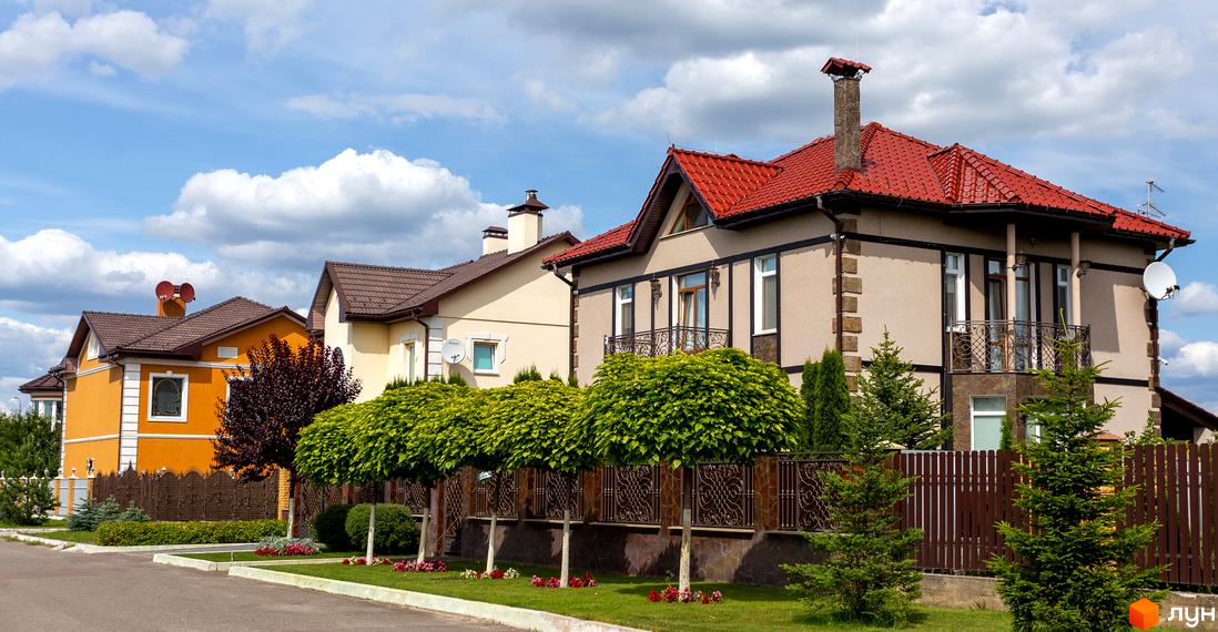 Котеджне містечко КМ Home Resort: фасади будинків з червоними та коричневими дахами, оранжевий будинок, зелені дерева та паркан. Прибудинкова територія з газоном та квітами.