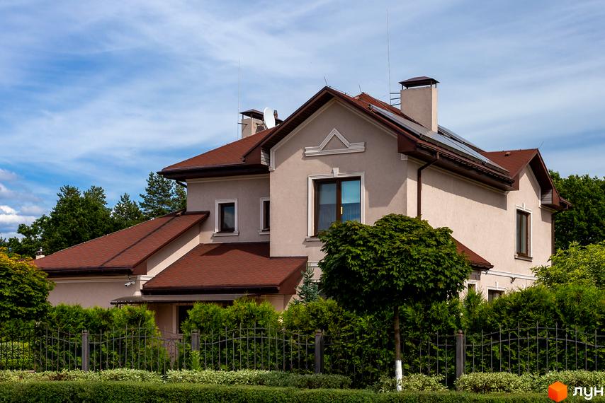 Котеджне містечко КМ Home Resort: двоповерховий будинок з коричневим дахом, вікнами та сонячними панелями. Доглянута прибудинкова територія з зеленими насадженнями та парканом.