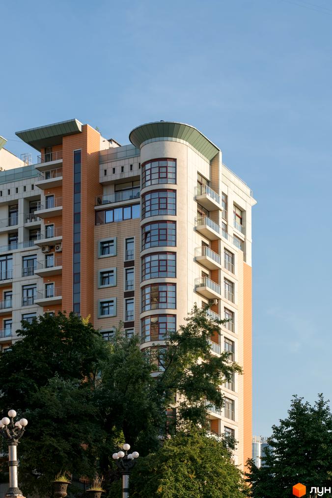 Житловий комплекс Капітолій - це сучасна багатоповерхова будівля з балконами та панорамними вікнами, оточена зеленню дерев.