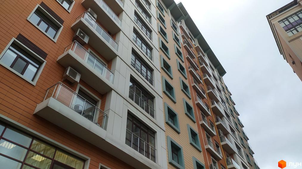 Фасад житлового комплексу Капітолій з балконами та кондиціонерами. Зовнішній вигляд новобудови з цегляним оздобленням.