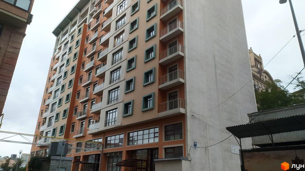 Зовнішній вигляд житлового комплексу Капітолій з цегляним фасадом та балконами. Навколо комплексу видно міську забудову та дерева.