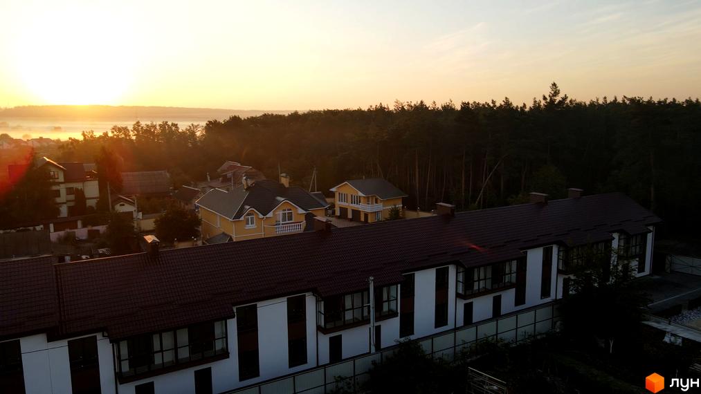 Таунхауси Green Heaven з коричневими дахами та білими фасадами на тлі лісу. Вид на будинки та прилеглу територію під час світанку.