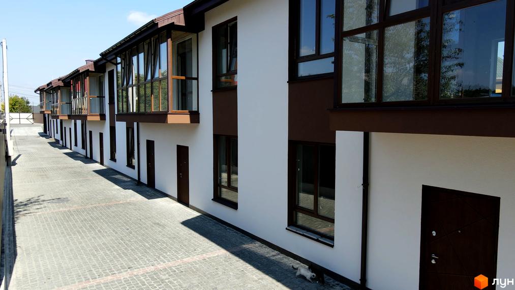 Зовнішній вигляд таунхаусів Green Heaven з коричневими вікнами та дверима, розташованих на вимощеній бруківкою території.