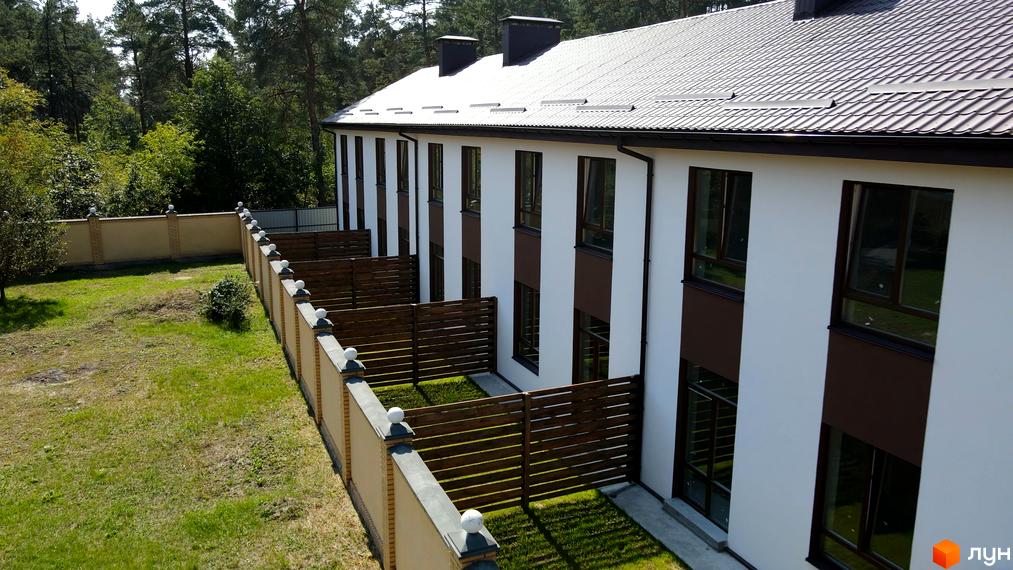 Таунхауси Green Heaven: ряд будинків з білими фасадами та коричневими акцентами, темними дахами. Прибудинкова територія з дерев'яними огорожами та парканом біля лісу.