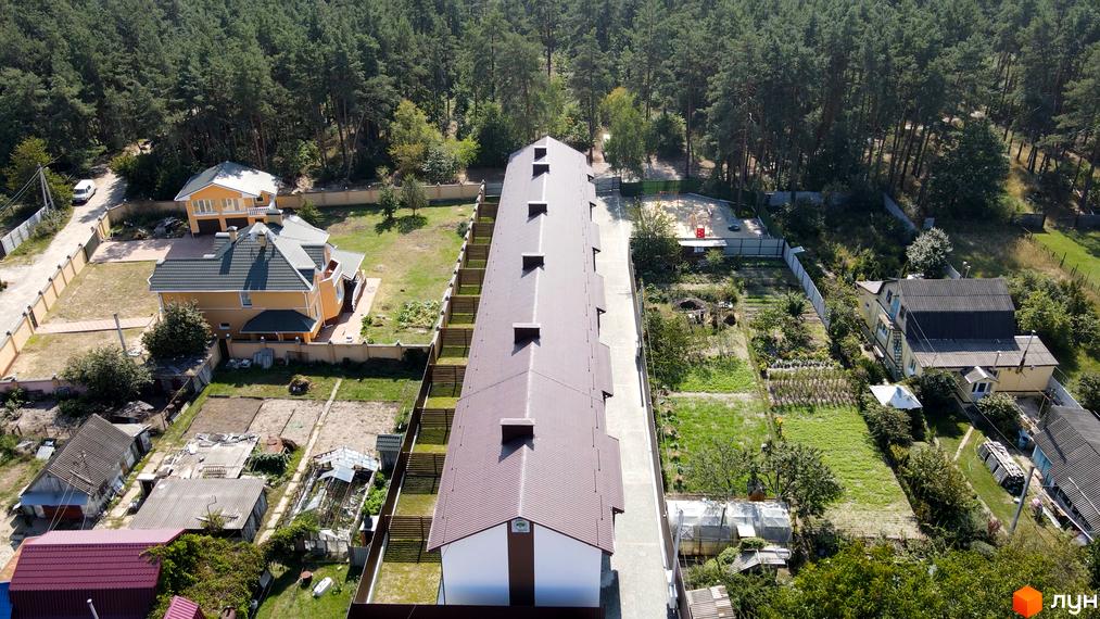 Таунхауси Green Heaven: вид зверху на довгу будівлю з коричневим дахом та світлим фасадом, оточену лісом та присадибними ділянками.