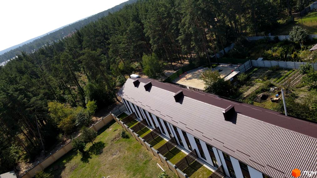 Таунхауси Green Heaven з коричневим дахом та білими стінами, оточені зеленою зоною та лісом. На території є дитячий майданчик та сад.