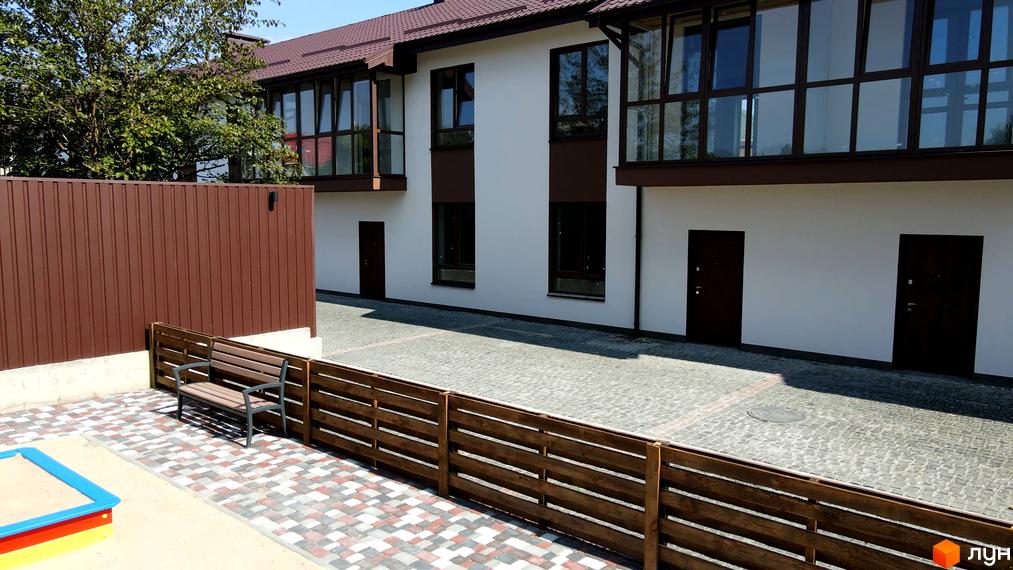 Таунхауси Green Heaven з білими фасадами та коричневими вікнами. Прибудинкова територія має бруківку, лавку та дитячу пісочницю.