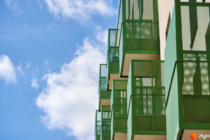 Зелені балкони житлового району Rybalsky на фоні блакитного неба з хмарами. Зовнішній вигляд будівель з оригінальними архітектурними елементами.