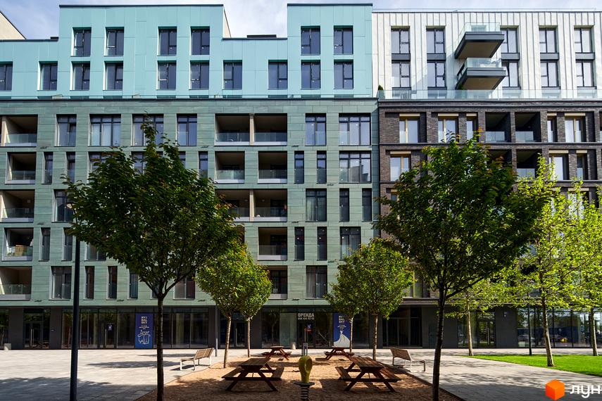 Житловий район Rybalsky: фасади будинків з блакитними та зеленими панелями, балконами та великими вікнами. Прибудинкова територія з деревами, лавками та зонами відпочинку.