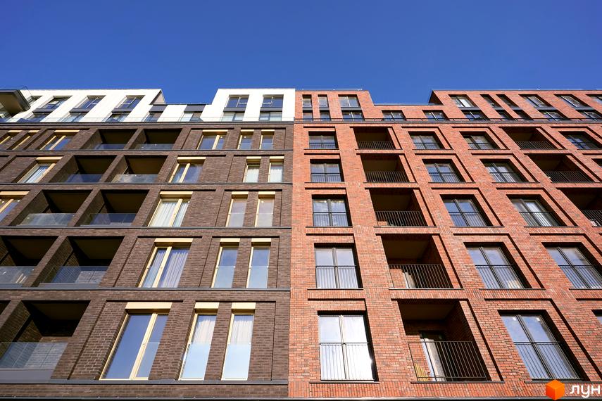 Фасад житлового комплексу Rybalsky з цегляною обробкою та великими вікнами. Сучасна архітектура новобудови під блакитним небом.