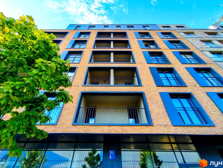 Фасад житлового району Rybalsky з цегляним оздобленням та синіми віконними рамами. Зелене дерево біля будівлі.