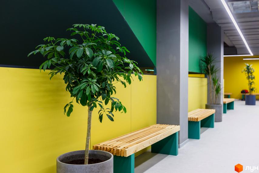 Житловий район Rybalsky: зелені насадження та дерев'яні лавки в зоні відпочинку біля жовтої стіни. Сучасне оздоблення фасаду та освітлення.