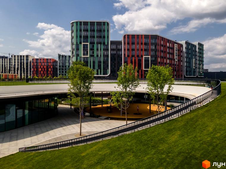 Багатоповерхові будинки Житлового комплексу Respublika з фасадами зеленого, червоного та чорного кольорів, із заокругленими кутами. На передньому плані зелені газони та дитячий майданчик.