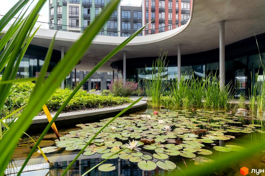 Житловий комплекс Respublika з багатоповерховими будинками та великим ставком з лататтям і зеленими насадженнями на прибудинковій території.