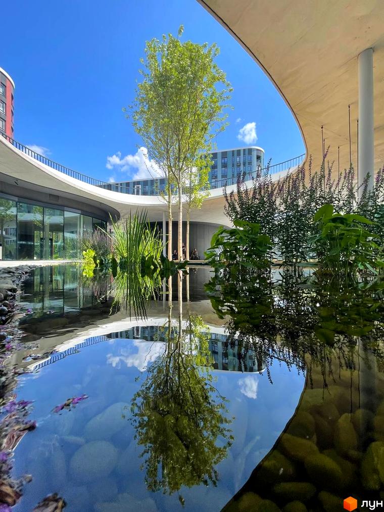 Житловий комплекс Respublika: вигнута будівля з панорамними вікнами та внутрішній двір з водоймою, деревами та рослинами.