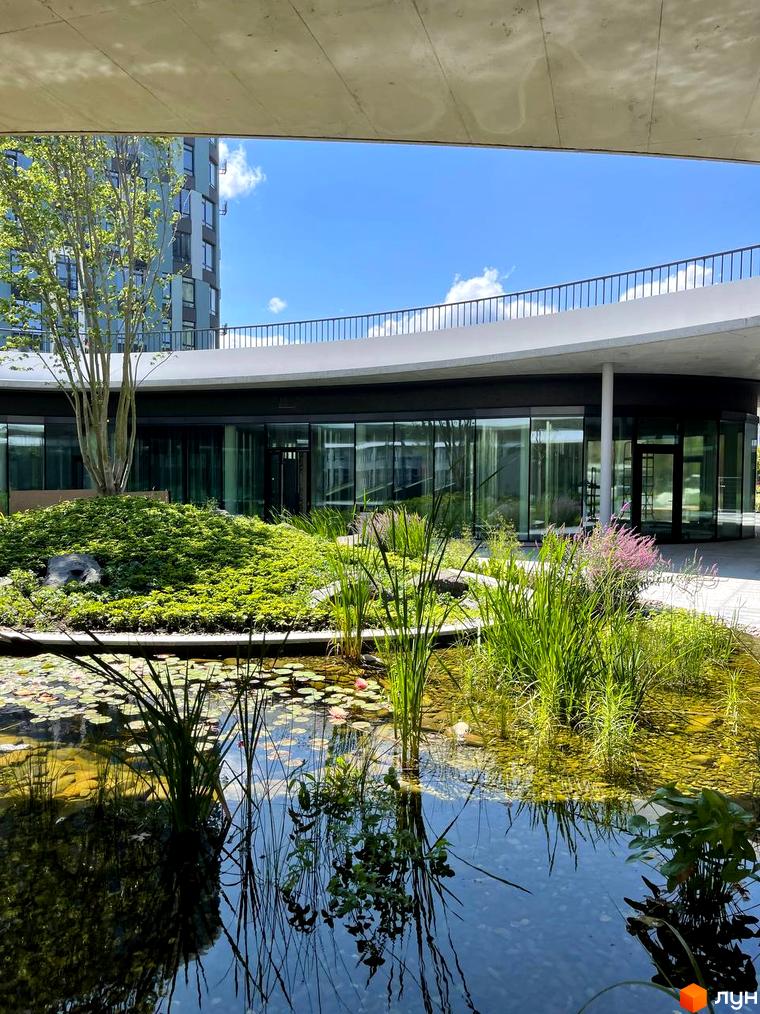 Житловий комплекс Respublika: будівля зі скляними фасадами та округлою архітектурою. На прибудинковій території ставок з лататтям та зелені насадження.