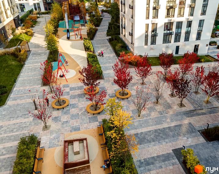 Житловий комплекс Файна Таун: білий багатоповерховий будинок та облаштована територія з осінніми деревами та дитячими майданчиками.