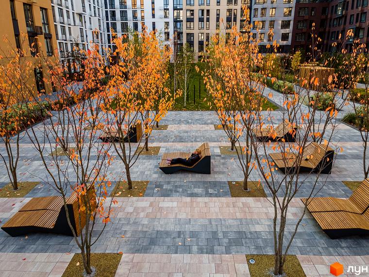 Багатоповерхові будинки Житлового комплексу Файна Таун з різнокольоровими фасадами та доглянута прибудинкова територія з осінніми деревами, мощенням і лавами для відпочинку.