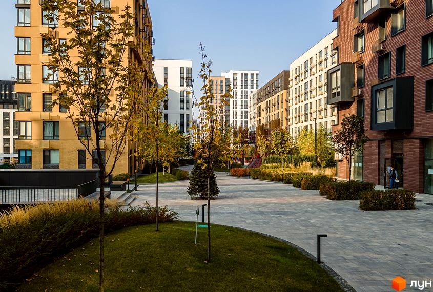 Житловий комплекс Файна Таун з багатоповерховими будинками жовтого, білого та коричневого кольорів. Двір облаштований газонами, деревами та вимощеними доріжками.