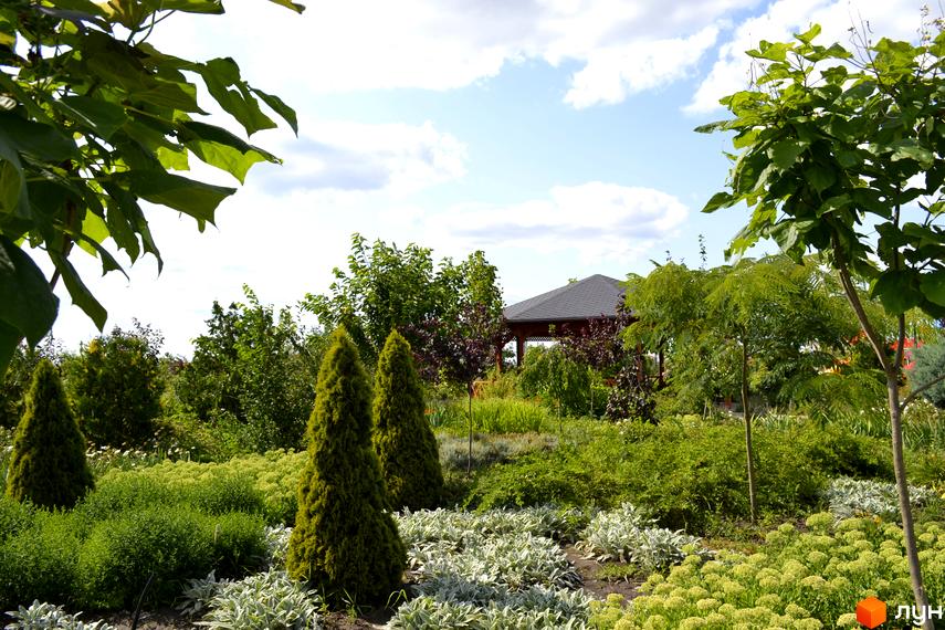 Ландшафтний дизайн Котеджного містечка Дайберг: доглянутий сад з хвойними та листяними деревами, кущами та альтанкою.