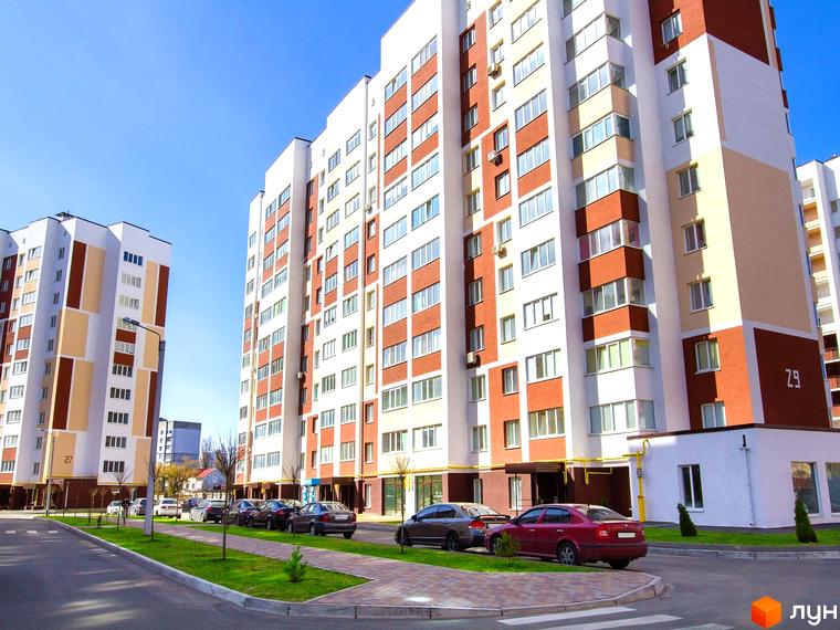 Зовнішній вигляд житлового комплексу Сади Вишневі з фасадами білого, коричневого та бежевого кольорів. Прибудинкова територія з зеленими насадженнями та припаркованими автомобілями.