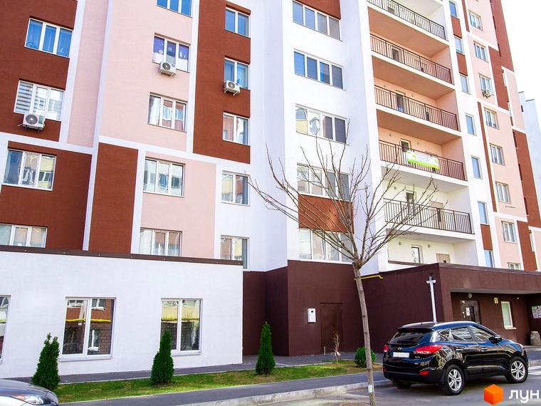 Житловий комплекс Сади Вишневі: фасади будівель з коричневими та рожевими елементами, балкони, вікна, прибудинкова територія з деревами та автомобілем.