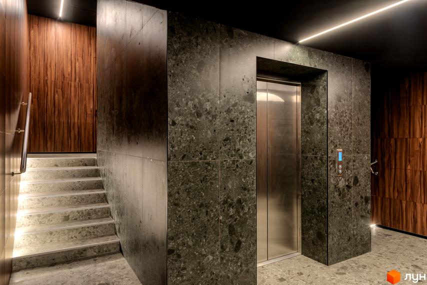 Інтер'єр будинку з ліфтом та сходами з сірого каменю. Стіни оздоблені темним деревом та кам'яною плиткою. Освітлення - світлодіодна стрічка.