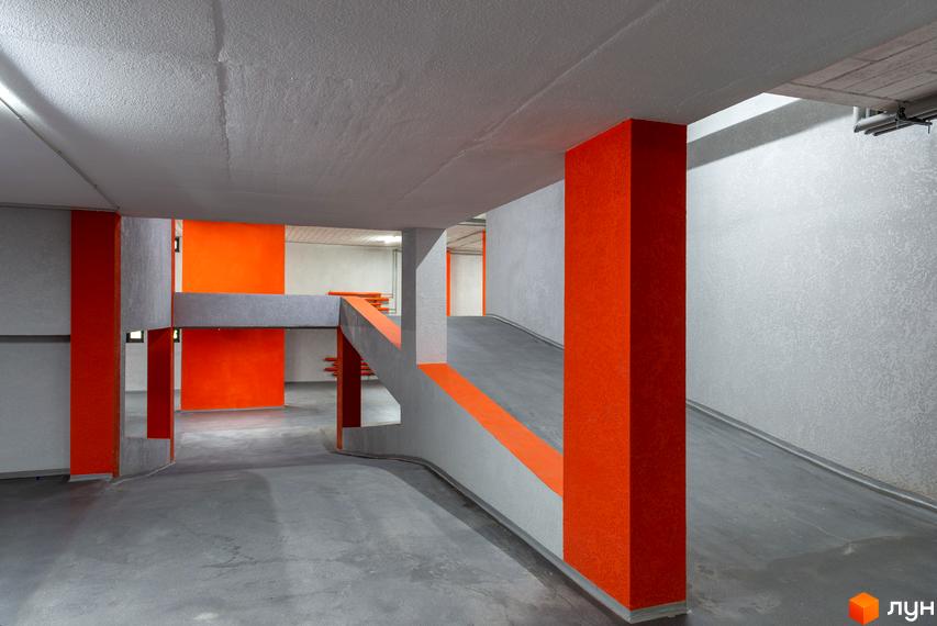 Інтер'єр паркінгу в клубному будинку Hidden з бетонними стінами та яскравими помаранчевими акцентами, що створюють цікавий візуальний ефект.