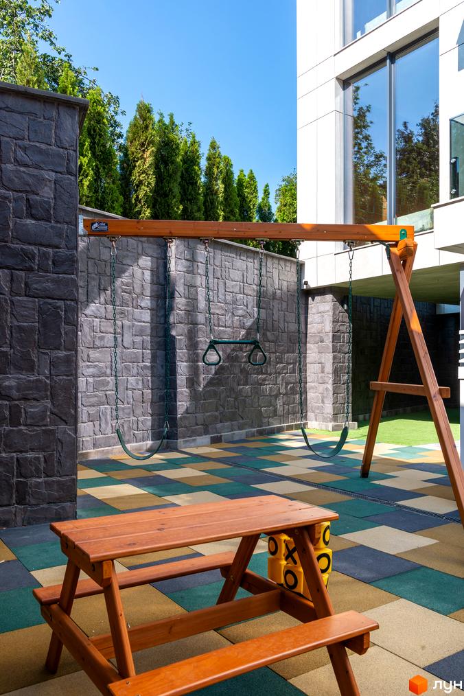 Житловий комплекс Hidden з дитячим майданчиком та зоною відпочинку. Фасад будинку з великими вікнами, оздоблений декоративним каменем.