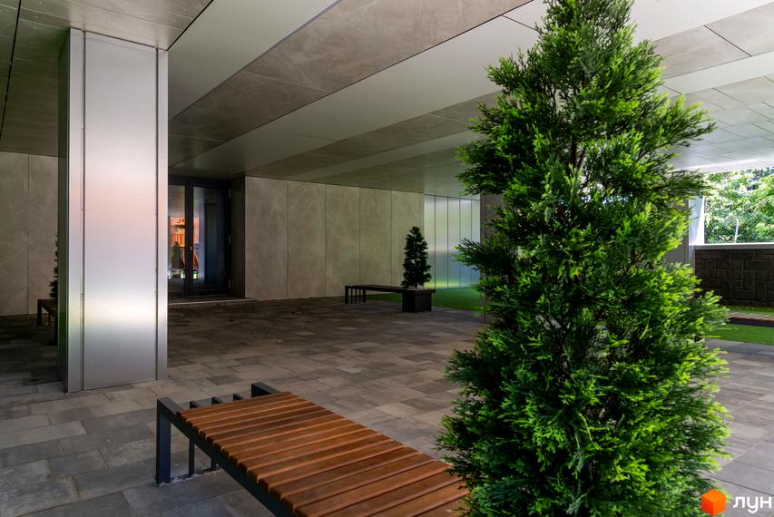 Вхідна група в ЖК Hidden з оздобленням з каменю та дерева. На території розташовані лавки та зелені насадження.