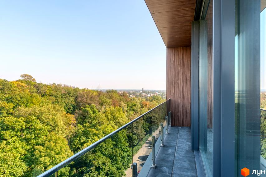Вид з балкону Клубного будинку Hidden: скляні перила, панорамні вікна, оздоблення деревом. Навкруги зелені дерева та місто на горизонті.