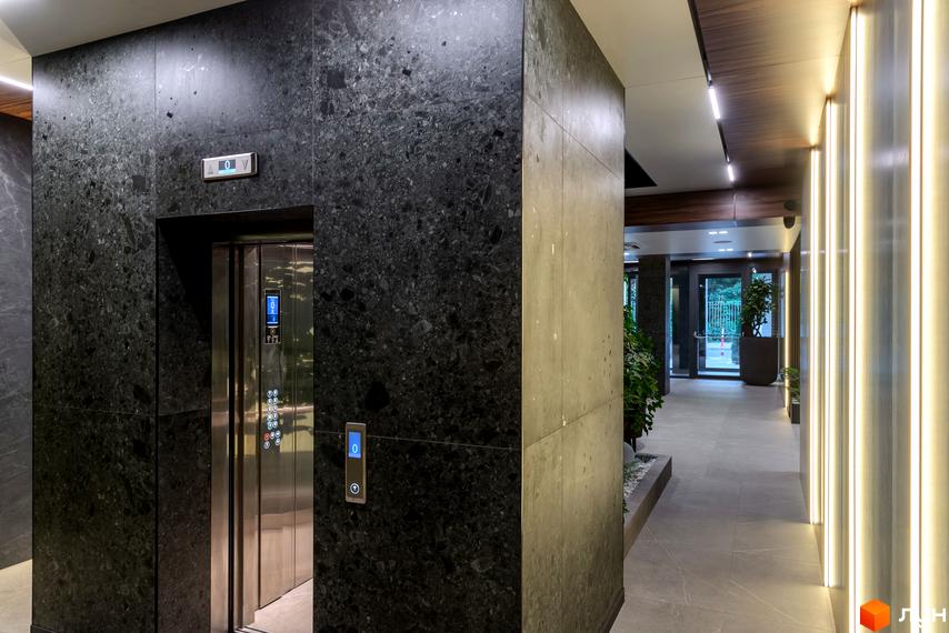 Інтер'єр холу в клубному будинку Hidden з ліфтом та оздобленням з каменю. Просторий коридор з підсвічуванням та рослинами.