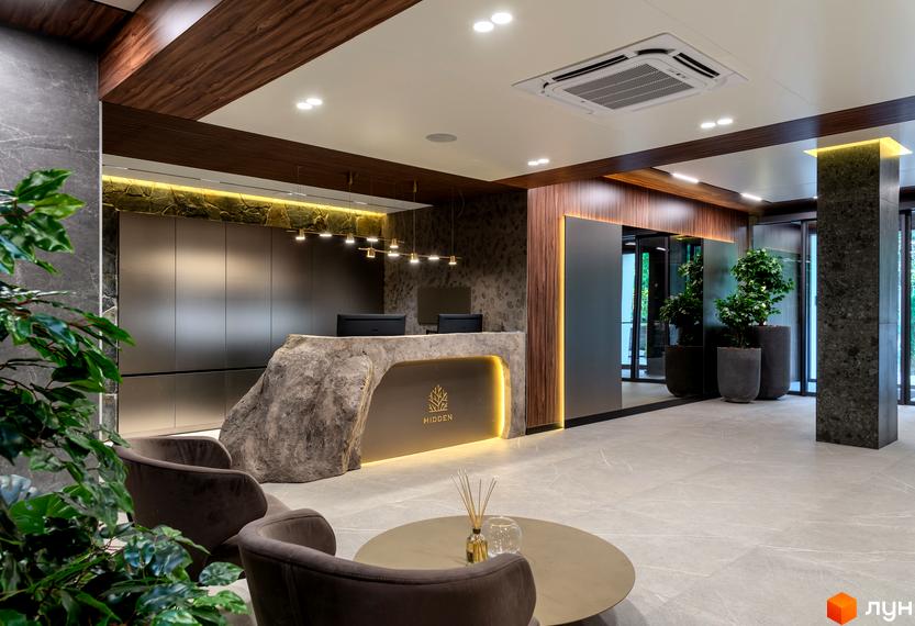 Інтер'єр холу в клубному будинку Hidden з кам'яною стійкою ресепшен, м'якими кріслами, рослинами та круглим столиком. Світлий простір з акцентами на натуральних матеріалах.