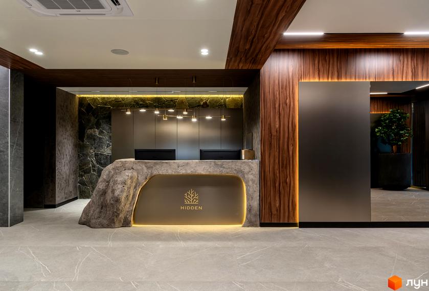 Ресепшн в клубному будинку Hidden з кам'яним дизайном. Світлий інтер'єр з дерев'яними панелями та рослинами.