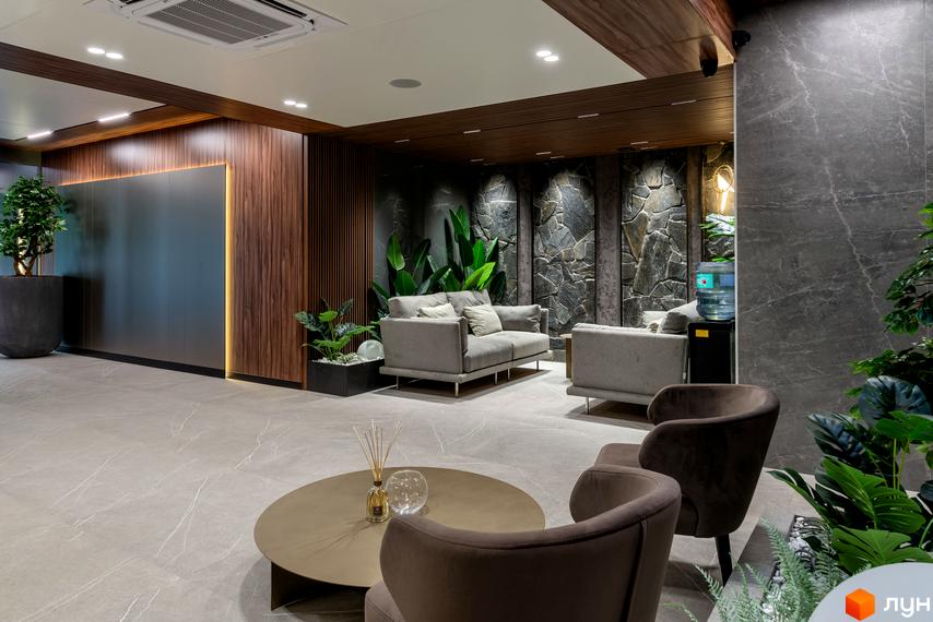Інтер'єр холу в клубному будинку Hidden: сірі дивани, крісла, столик, рослини, оздоблення стін деревом та каменем, велика світла підлога.