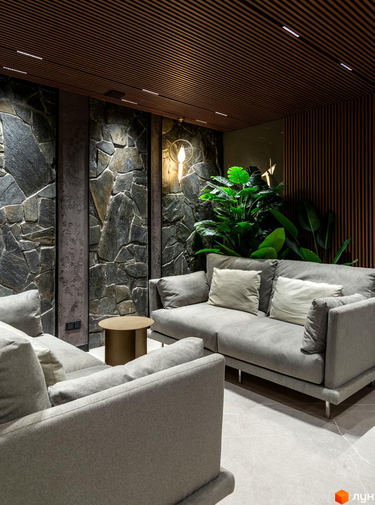 Інтер'єр вітальні в клубному будинку Hidden з кам'яною стіною, диваном та рослинами. Дизайн квартири в новобудові.