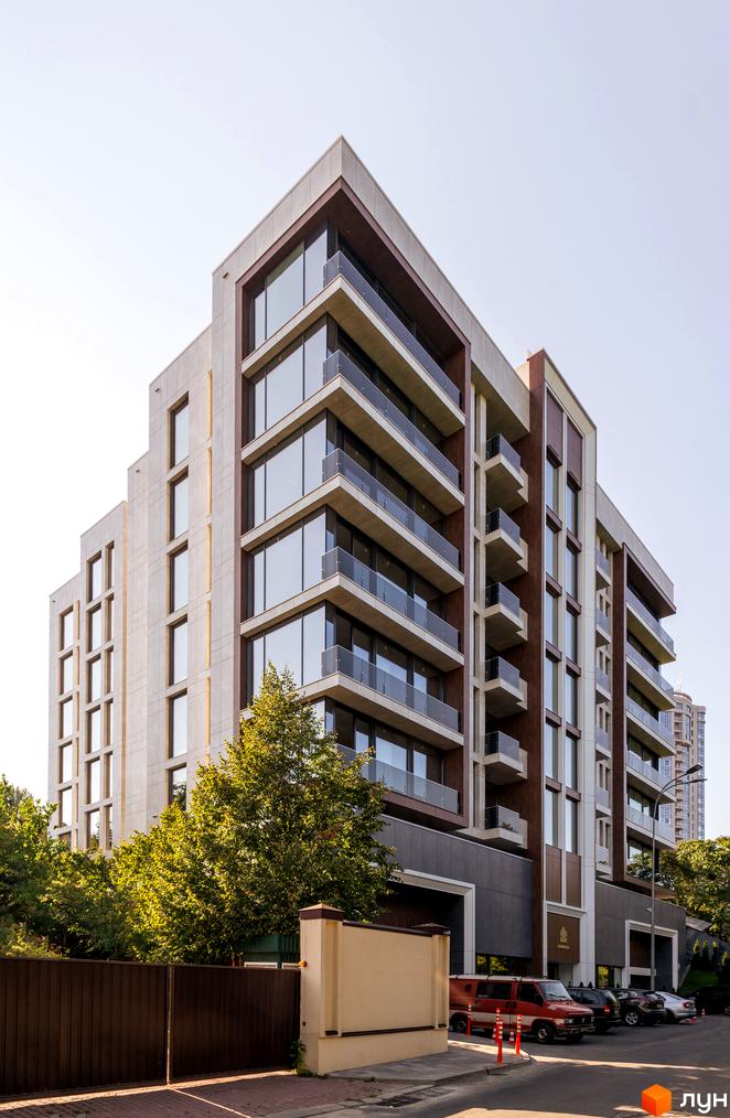 Висотна будівля Клубний будинок Hidden з панорамними вікнами та балконами. На прибудинковій території розташовані дерева, паркан та автомобілі.