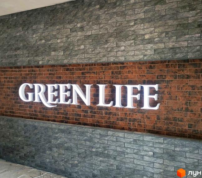 Новобудова Green Life-3 з білою об'ємною вивіскою на цегляній стіні. Фасад будинку оздоблений комбінацією цегли двох кольорів.