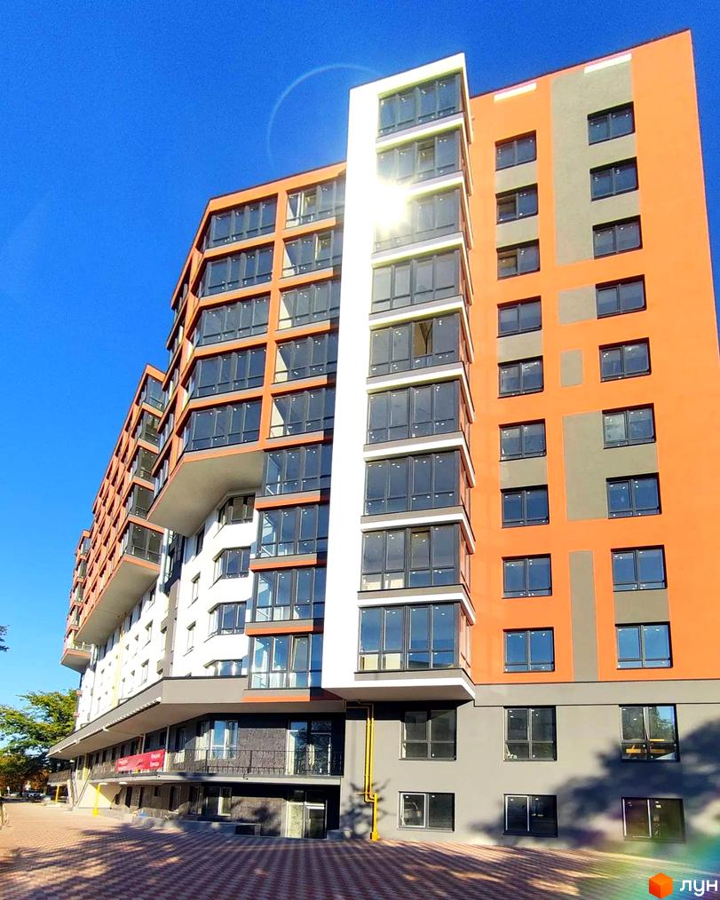 Новобудова ЖК Green Life-3 з яскравим фасадом та великими вікнами. Навколо будинку облаштована прибудинкова територія з бруківкою та зеленими насадженнями.