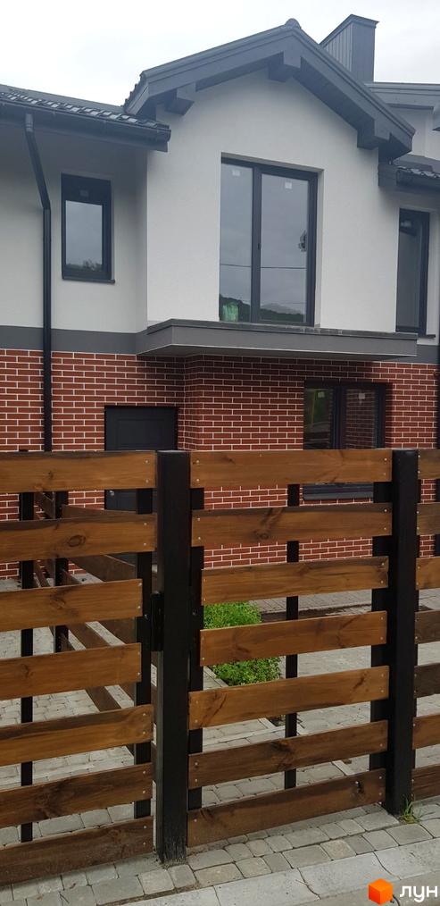 Зовнішній вигляд будинку КМ Скандинавія з цегляним фасадом та дерев'яним парканом. Фото новобудови.