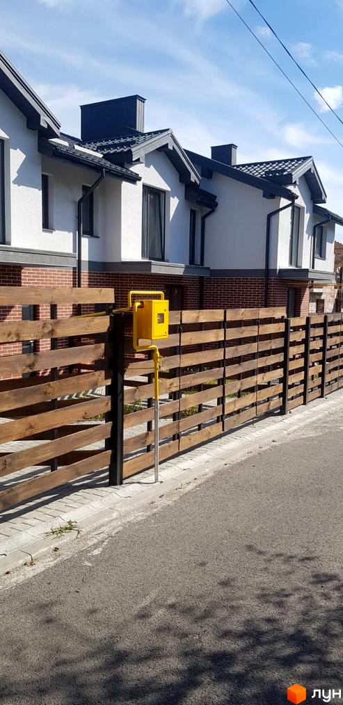 Зовнішній вигляд будинків комплексу КМ Скандинавія з дерев'яним парканом та газовим лічильником. Новобудова з цегляним цоколем та білими стінами.