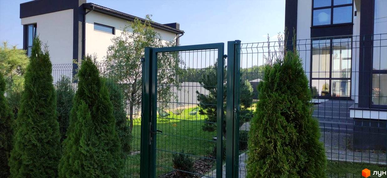 Зовнішній вигляд котеджного містечка КМ Tivoli з зеленими туями та парканом. Територія комплексу з газоном та деревами.