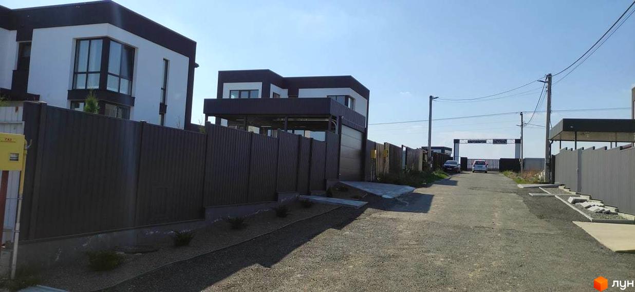 Котеджне містечко Tivoli: двоповерхові будинки з чорними дахами та білими стінами, огороджені парканом, на фоні блакитного неба.