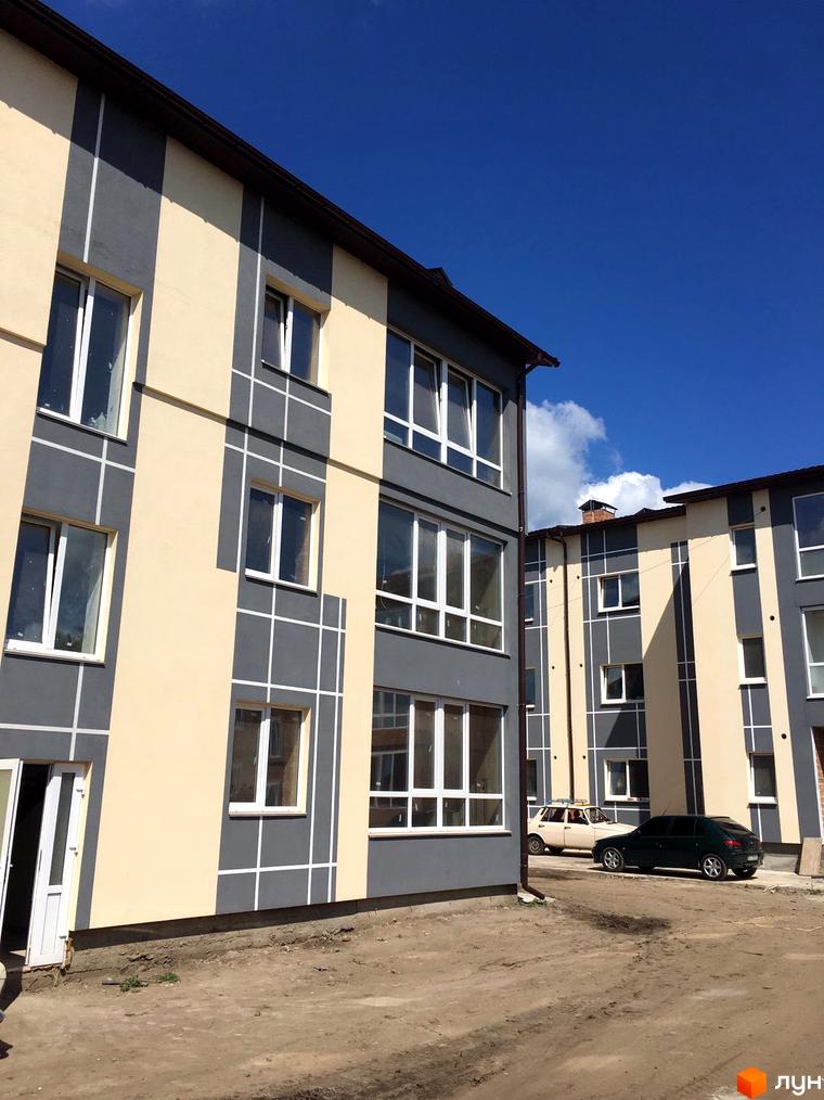Зовнішній вигляд новобудови ЖК Flat city з сірими та бежевими фасадами, вікнами та прибудинковою територією з автомобілями.