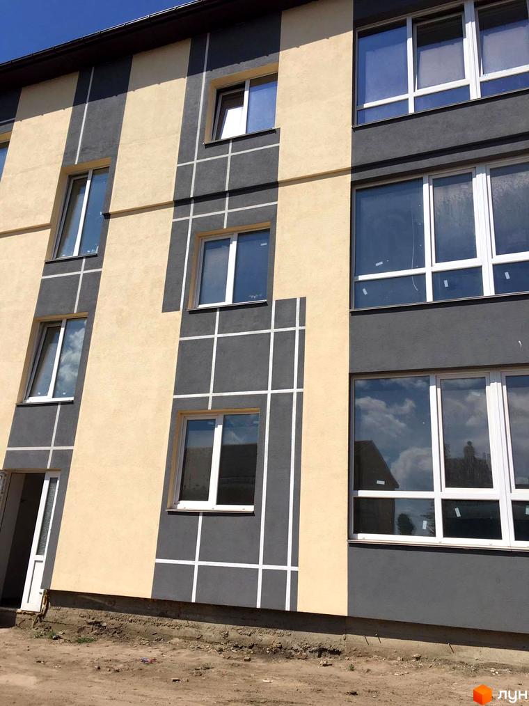 Фасад новобудови ЖК Flat city з вікнами та сірими та бежевими елементами. Навколо будівельний майданчик.