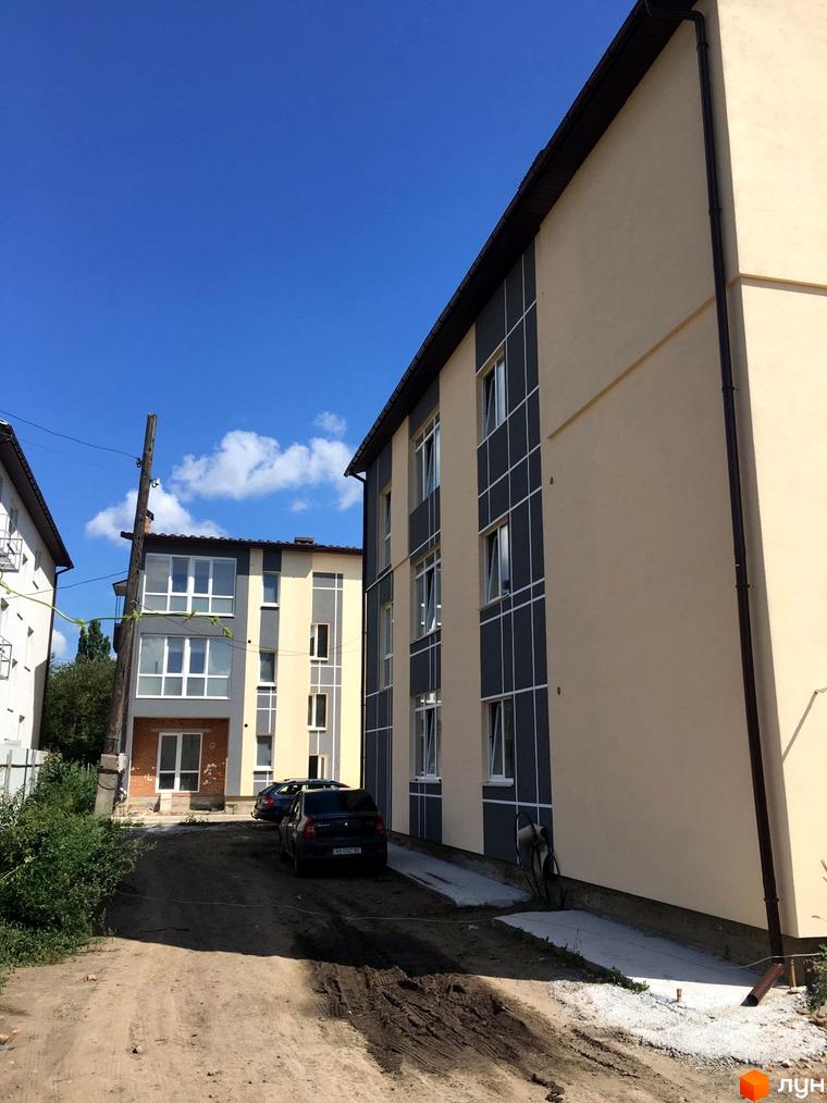 Житловий комплекс Flat city. Зовнішній вигляд будівель з сірими та бежевими фасадами, вікнами та прибудинковою територією з дорогою.