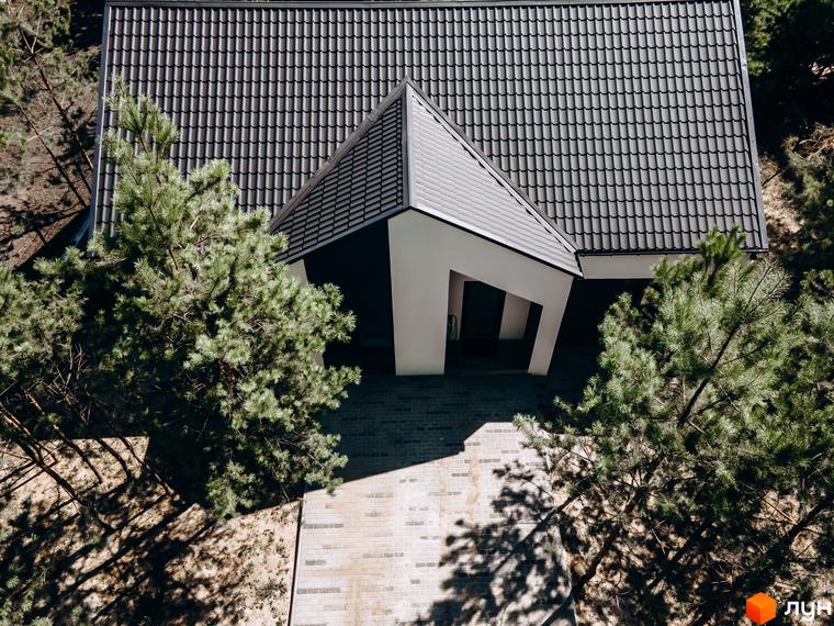 Котеджне містечко КМ Chaletville: вид зверху на будинок з темним дахом та білим фасадом, оточений соснами. Прибудинкова територія вимощена плиткою.