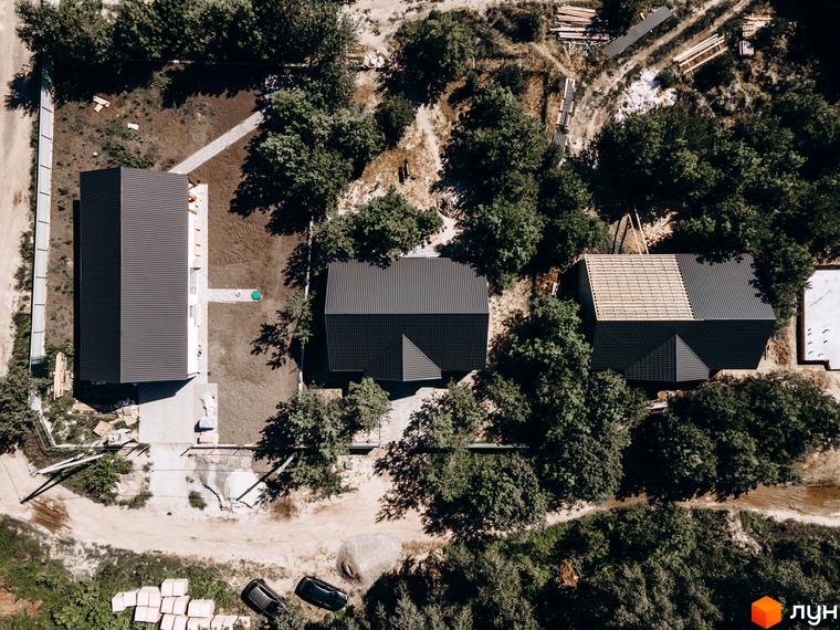 Аерофотографія Котеджного містечка Chaletville: будинки з темними дахами та світлими фасадами, на території з деревами та будівельними роботами.